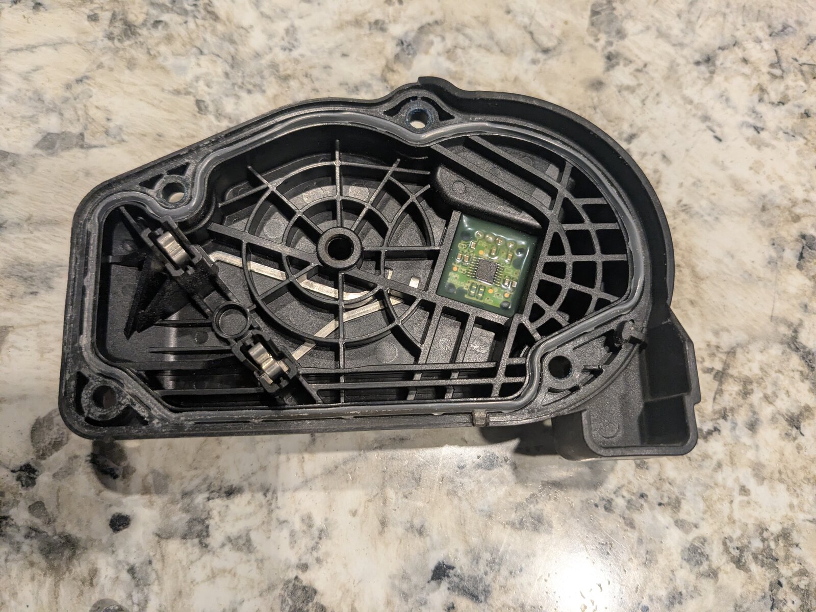 Interior of the motor housing cover, showing a small green circuit board with a Hall-effect sensor chip mounted opposite the gear train, plus two spring contacts.