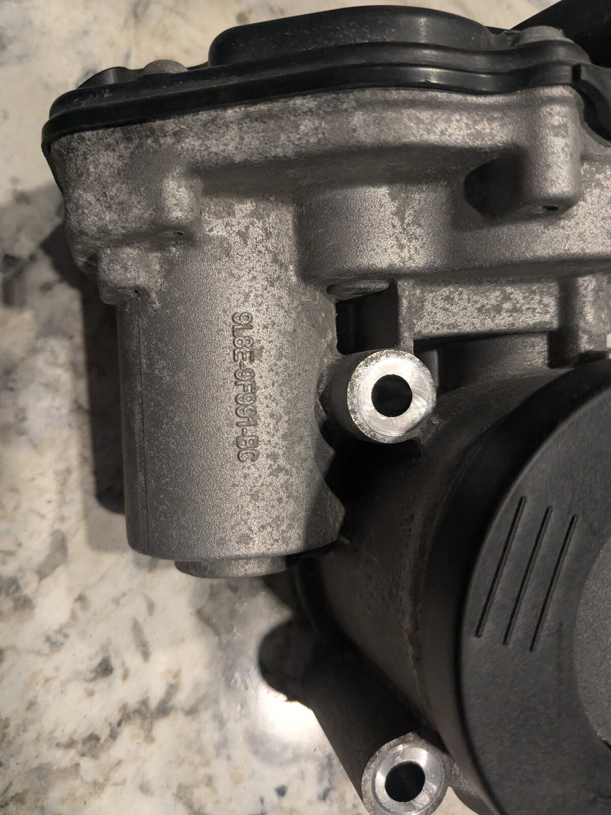Side view of the aluminum throttle body housing showing the same 9L8E-9F991-BC casting number stamped into the metal, next to the intake bore and throttle plate.