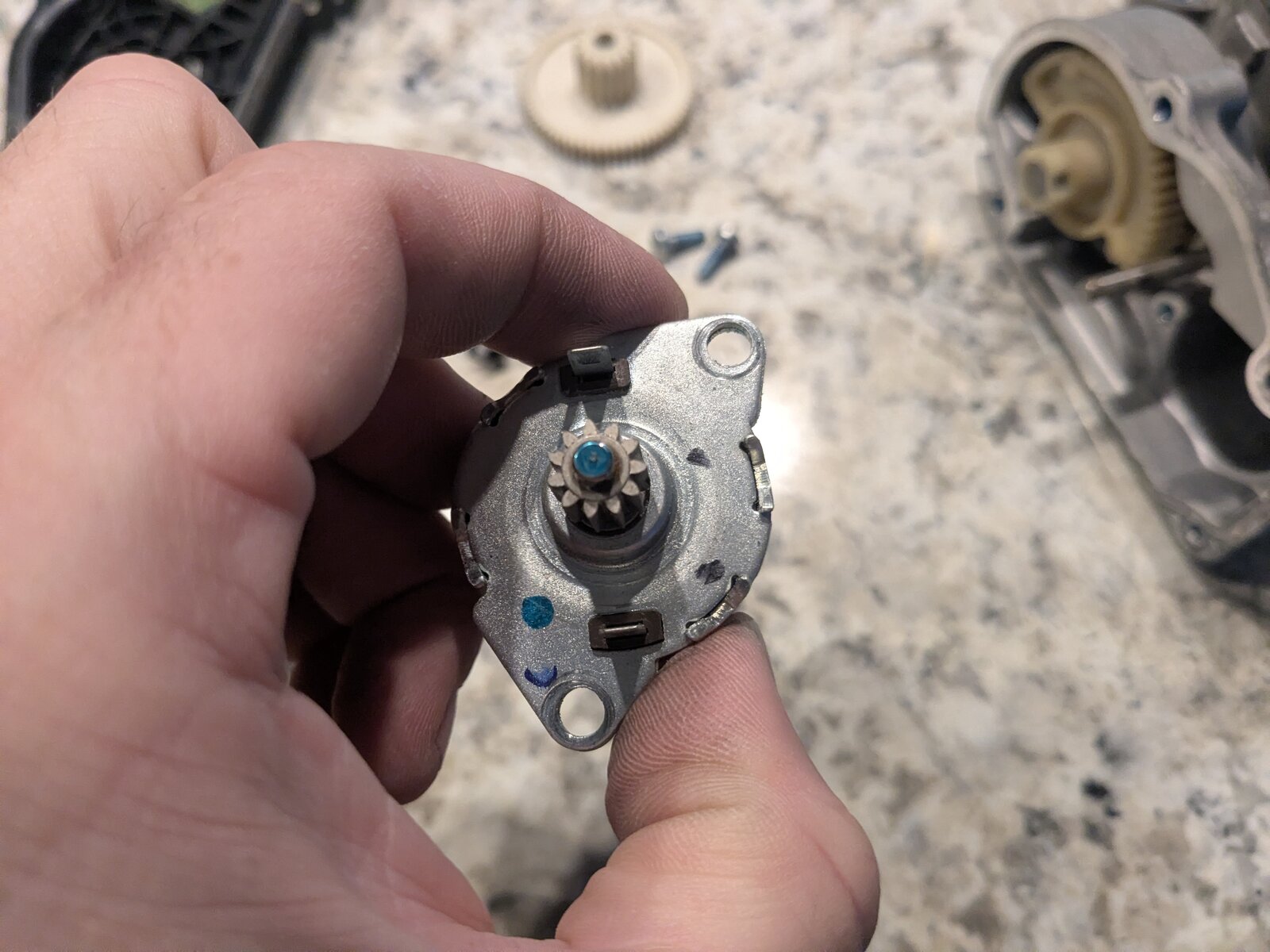 End view of the actuator motor's commutator, showing the brush contacts and commutator segments inside the black end cap, with visible dark discoloration consistent with contact wear.